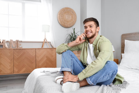 Young bearded man talking by mobile phone in bedroomの写真素材