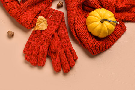 Gloves with scarf and autumn decor on beige background