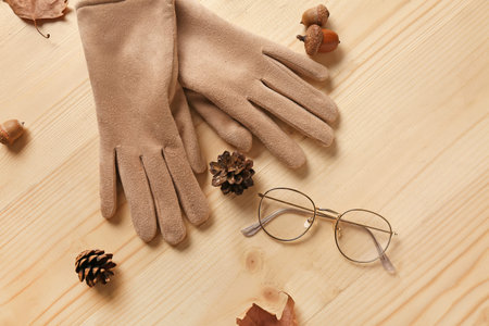 Gloves with eyeglasses and autumn decor on light wooden background