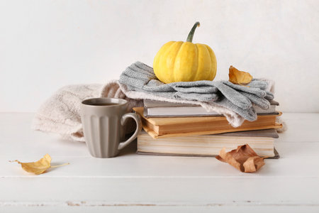 Cup of tea with gloves, scarf and books on wooden table against white backgroundの写真素材