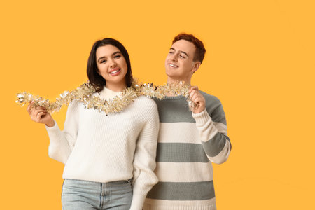 Young couple with Christmas tinsel on yellow backgroundの写真素材