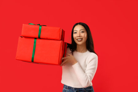 Young Asian woman with Christmas gift boxes on red backgroundの写真素材