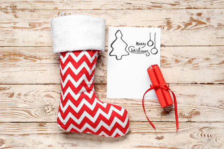 Christmas sock with greeting card and gift box on white wooden background