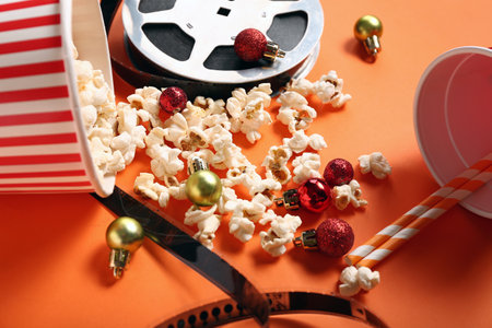 Bucket of popcorn with cup, film reel and Christmas balls on orange backgroundの写真素材