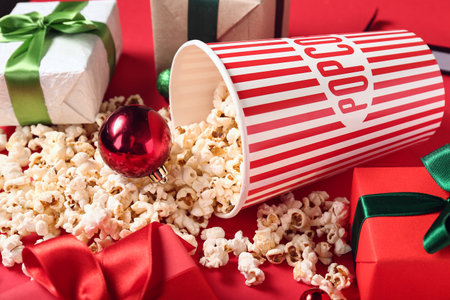 Bucket of popcorn with Christmas balls and gifts on red backgroundの写真素材