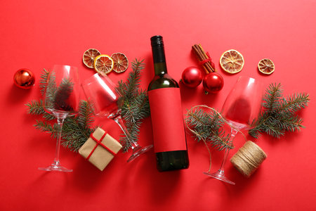 Bottle and glasses of wine with Christmas tree branches on red backgroundの写真素材