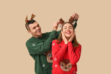 Beautiful young couple in reindeer horns on beige backgroundの写真素材