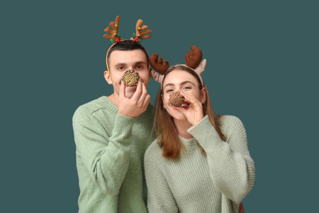 Beautiful young couple in reindeer horns with pine cones on green backgroundの写真素材