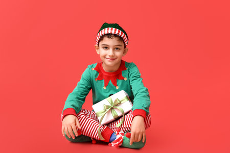 Cute little elf with Christmas gift on red backgroundの写真素材