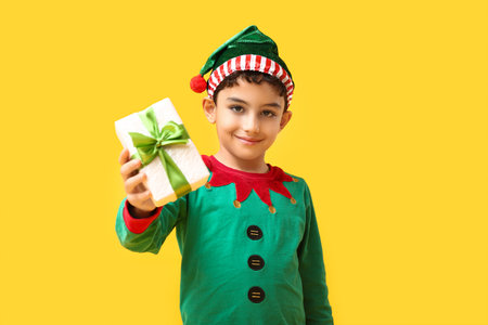 Cute little elf with Christmas gift on yellow backgroundの写真素材