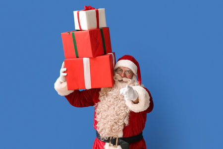 Santa Claus with Christmas gifts pointing at viewer on blue backgroundの写真素材