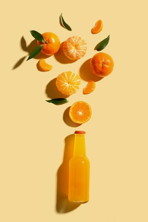 Sweet mandarins with leaves and bottle of juice on yellow backgroundの写真素材