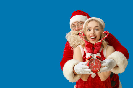 Happy people dressed as Santa Claus with alarm clock and candy canes on blue backgroundの写真素材