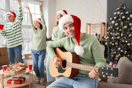 Young man playing guitar at Christmas party with his friendsの写真素材