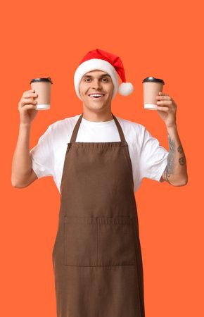 Male barista in Santa hat with cups of coffee on orange backgroundの写真素材