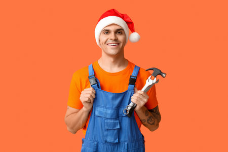 Male plumber in Santa hat with hammer and wrenches on orange backgroundの写真素材