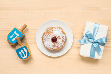 Plate with tasty donut, dreidels and gift for Hanukkah celebration on wooden backgroundの写真素材