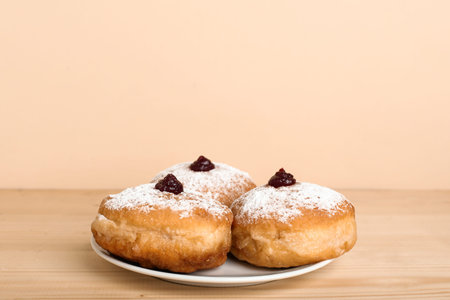 Plate with tasty donuts for Hanukkah celebration on wooden table against color background