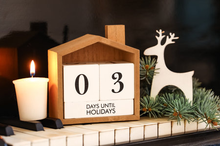 Calendar with text 3 DAYS UNTIL HOLIDAYS, burning candle and Christmas decorations on piano keys,...
