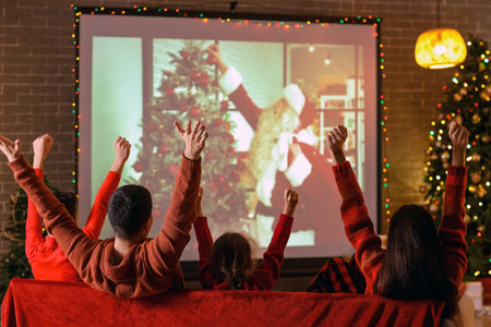 Happy family watching Christmas movie on projector screen at home, back viewの写真素材