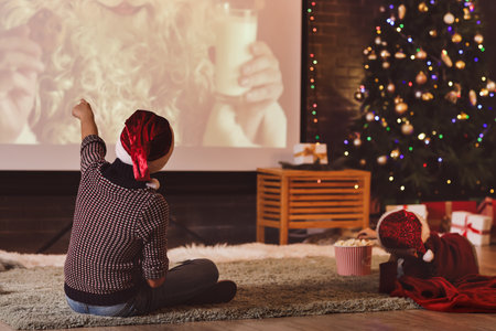 Little children with popcorn watching Christmas movie on projector screen at home, back viewの写真素材