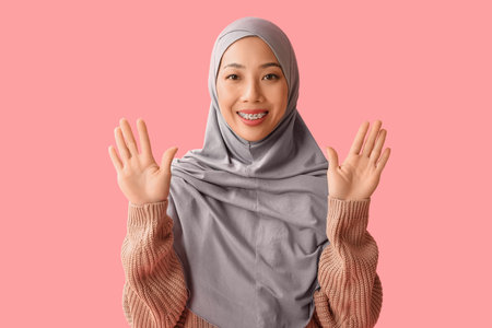 Beautiful young Muslim woman waving hands on pink backgroundの写真素材