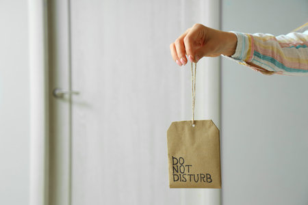 Woman with DO NOT DISTURB door hanger in hotel room, closeup