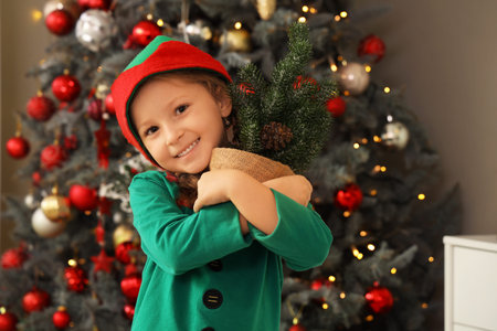 Cute little girl in elf costume with Christmas tree at home