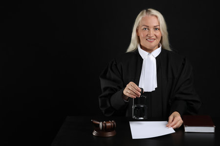 Mature female judge with stamp and document at table on black backgroundの写真素材