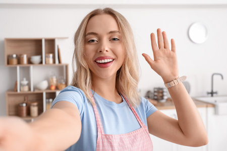 Beautiful young woman waving hand in kitchen at homeの写真素材