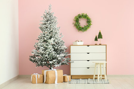 Beautiful Christmas tree with chest of drawers and gift boxes near pink wallの写真素材