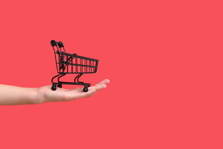 Female hand with black shopping cart on color background.の写真素材
