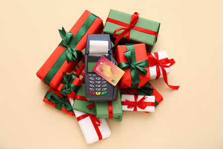 Payment terminal with credit card and Christmas gift boxes on yellow background