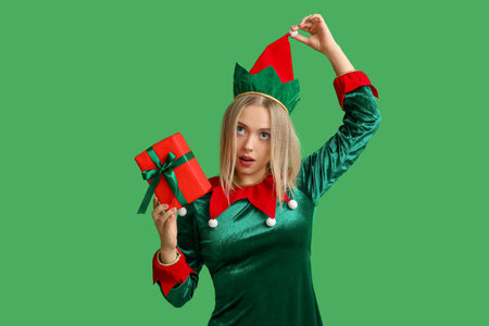 Young woman in elf costume with Christmas gift box on green backgroundの写真素材