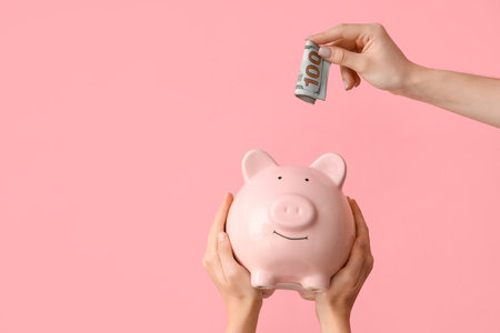 Female hands with piggy bank and money on pink backgroundの写真素材