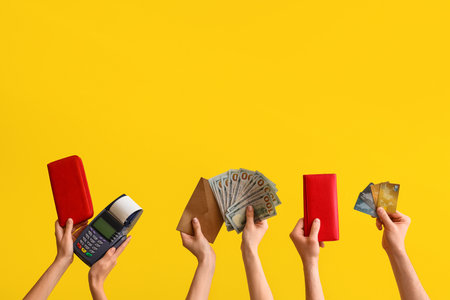 Female hands with wallets, payment terminal, credit cards and money on yellow backgroundの写真素材