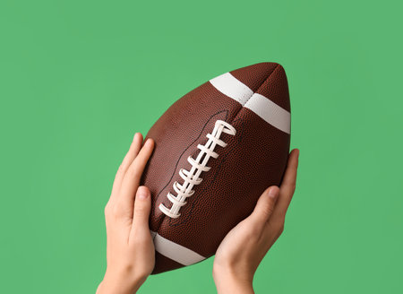 Female hands with ball for American football on green backgroundの写真素材