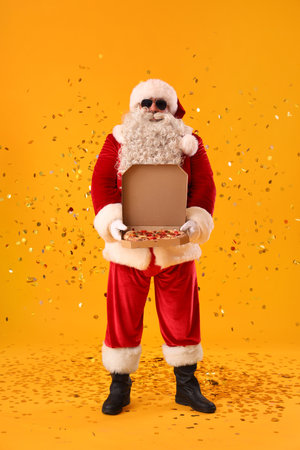 Cool Santa Claus with tasty pizza and confetti on yellow backgroundの写真素材