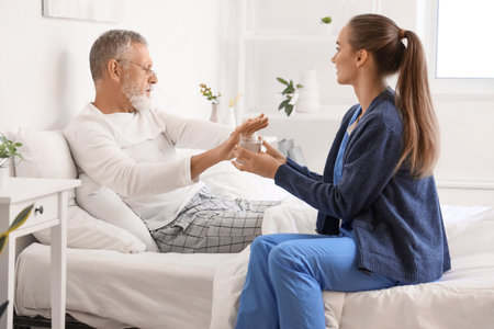 Senior man refusing to take pills from caregiver in bedroomの写真素材
