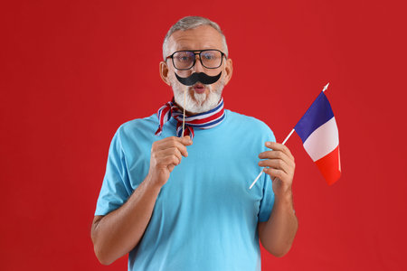 Senior man with paper mustache and flag of France on red backgroundの写真素材