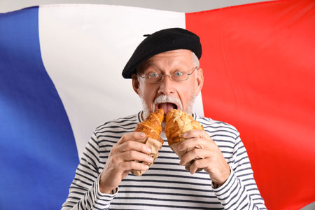 Senior man eating tasty croissants against flag of Franceの写真素材