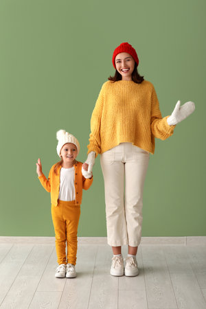 Young mother and her little daughter waving hands near green wallの写真素材