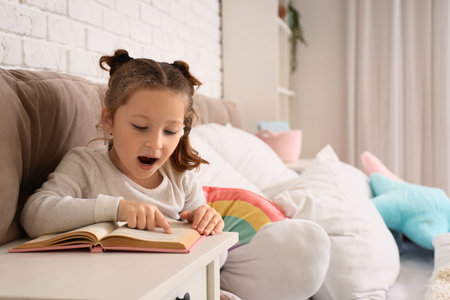 Cute little girl reading book in bedroomの写真素材