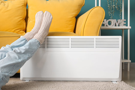 Young woman in warm winter socks near electric heater. Concept of heating seasonの写真素材