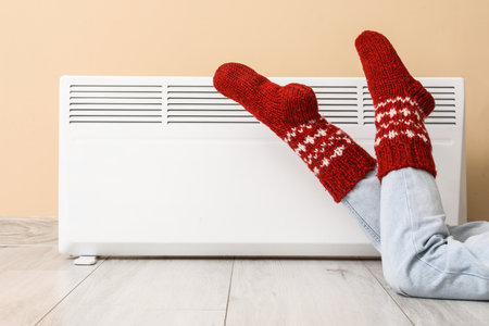 Woman in warm socks near electric heater at home. Concept of heating seasonの写真素材