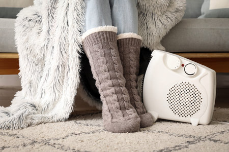 Young woman in winter socks with warm plaid near electric heater at home. Concept of heating seasonの写真素材