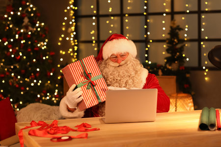 Santa Claus with laptop and Christmas gift at home