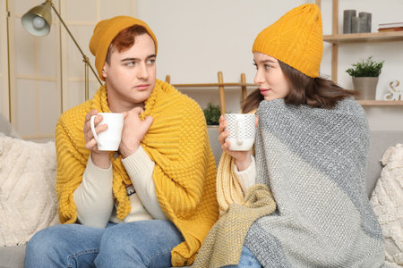 Frozen young couple drinking hot tea at home on winter dayの写真素材