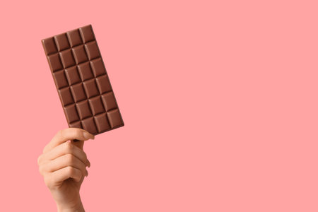 Female hand with chocolate bar on pink backgroundの写真素材