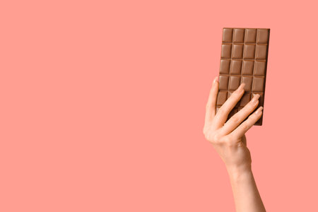 Female hand with chocolate bar on pink backgroundの写真素材